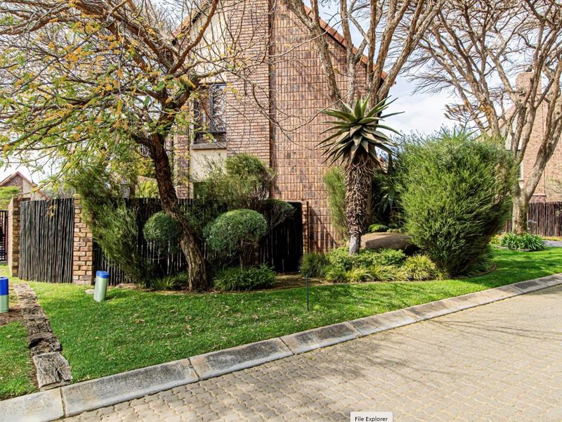 A view of the front exterior of the brick house, featuring a paved driveway, established garden, and timber fencing.