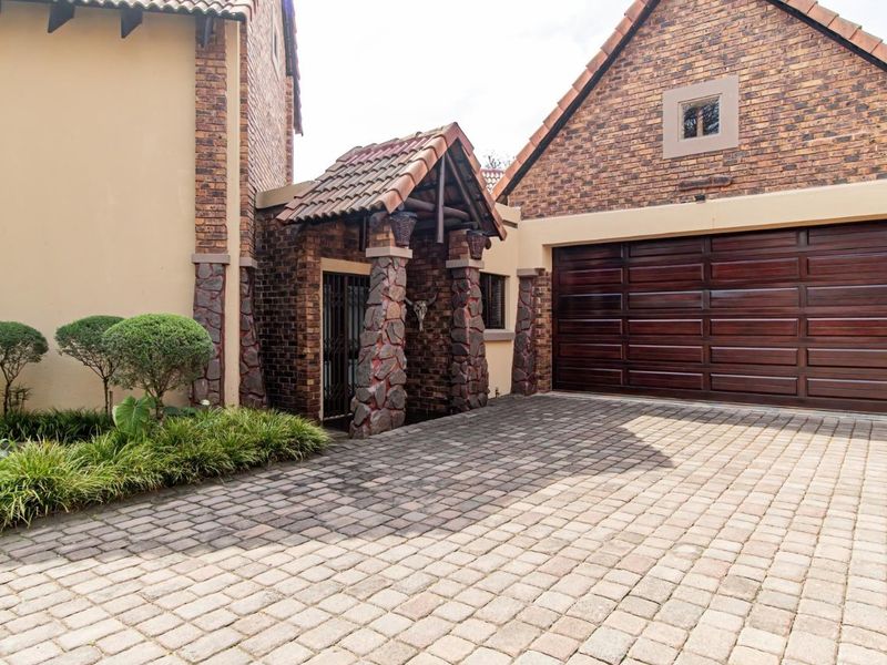 Front elevation of a house featuring a paved driveway, brick and stone facade, and a double garage door.