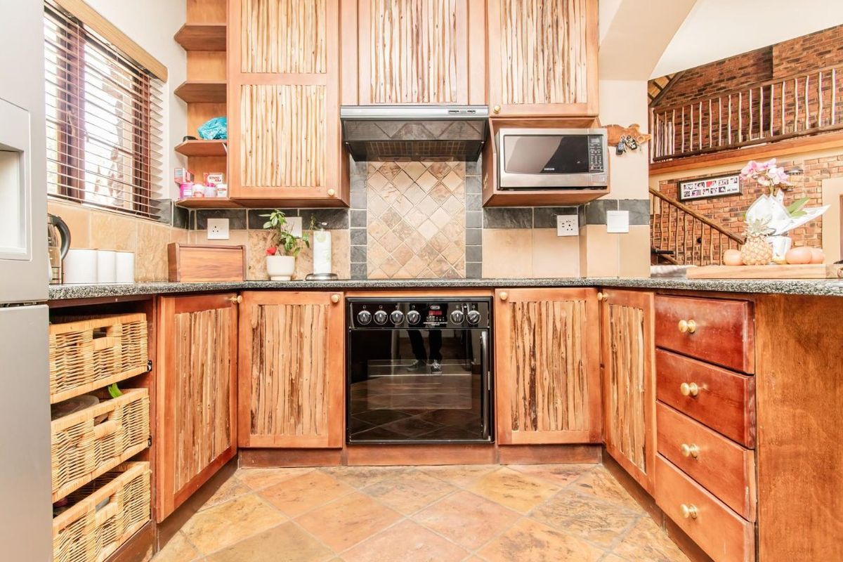 A rustic-style kitchen featuring wooden cabinetry, granite countertops, a built-in oven with extractor fan, and tiled flooring.