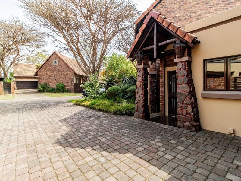 Front entrance view featuring a paved driveway, stone-clad pillars, and a covered porch area with a brick facade.