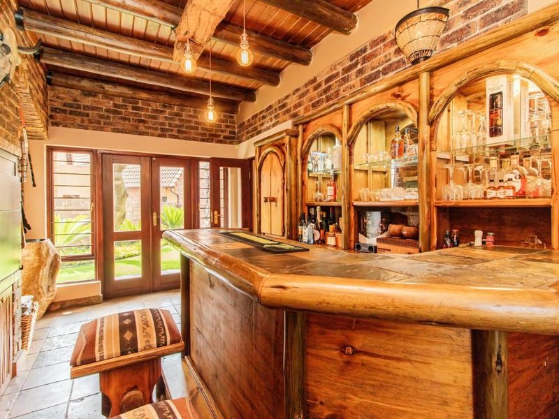 A rustic-style home bar featuring exposed brick walls, timber ceiling beams, a custom wooden bar counter, and direct access to the garden via french doors.