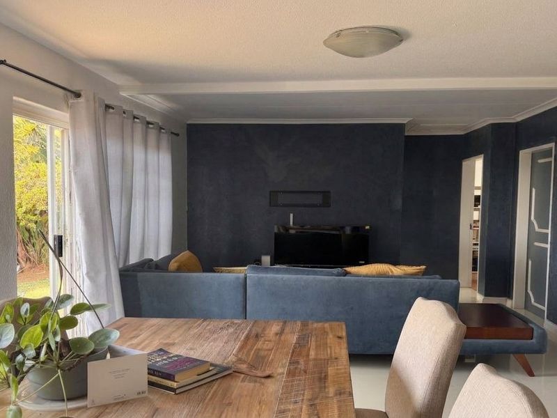 Open plan living and dining area featuring a sliding glass door to the garden and a modern dark feature wall.