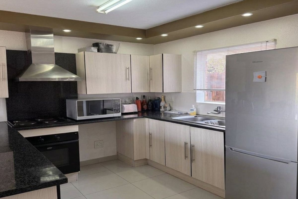 A functional kitchen featuring light wood-finish cabinetry, dark granite countertops, stainless steel appliances, and recessed ceiling lighting.