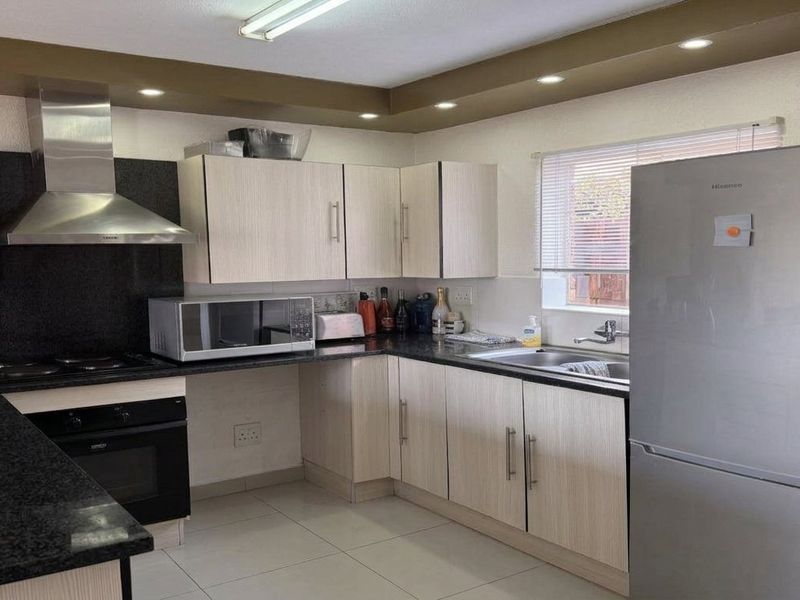 A functional kitchen featuring light wood-finish cabinetry, dark granite countertops, stainless steel appliances, and recessed ceiling lighting.