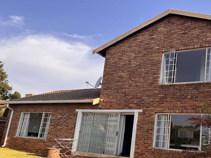 Rear view of a double-storey face brick townhouse featuring a tiled roof, sliding glass doors with security gates, and established garden surroundings.