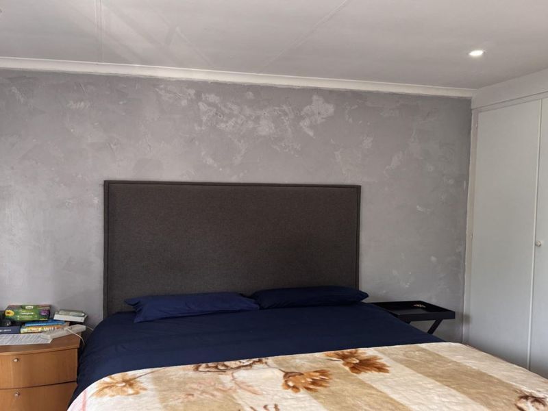 A bedroom featuring a textured grey feature wall, built-in wardrobe storage, and recessed ceiling lighting.