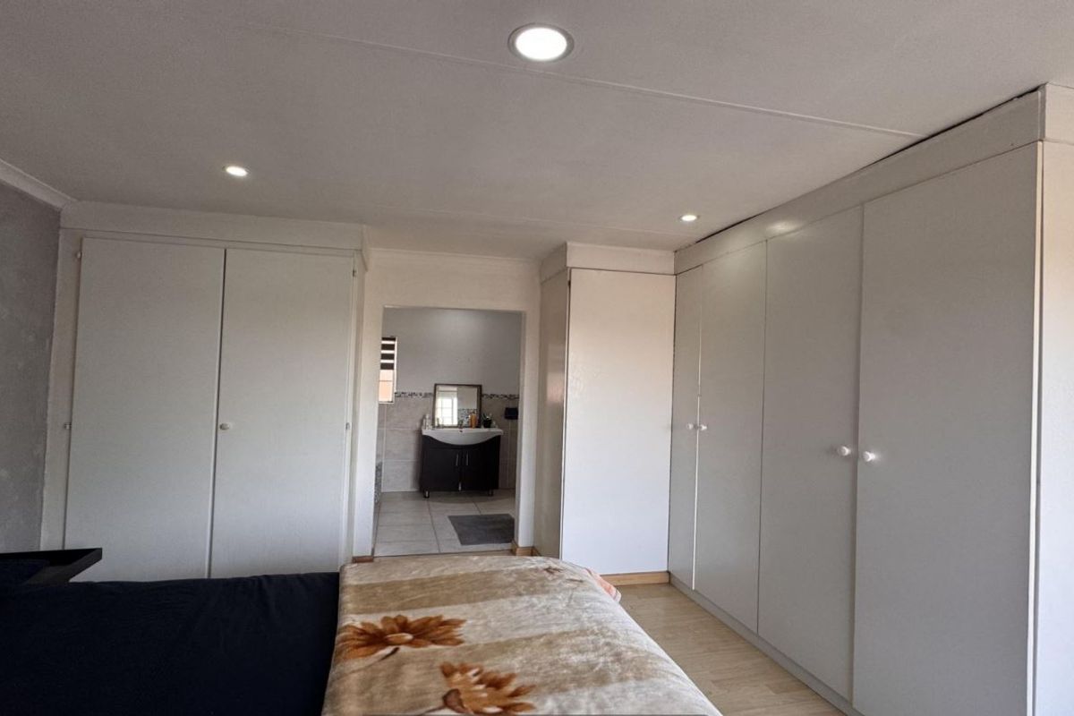 Spacious bedroom featuring extensive built-in cupboards, modern recessed downlighting, and laminate flooring, with convenient access to an adjoining en-suite bathroom.