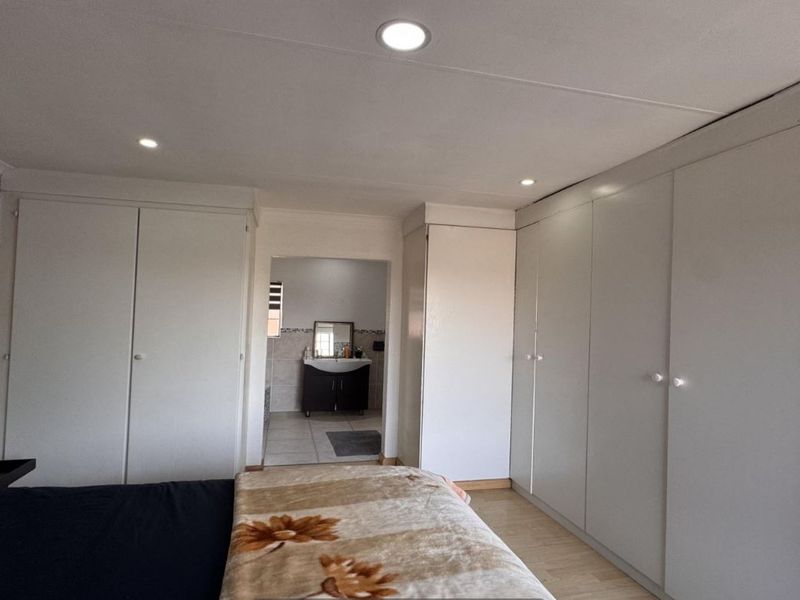 Spacious bedroom featuring extensive built-in cupboards, modern recessed downlighting, and laminate flooring, with convenient access to an adjoining en-suite bathroom.
