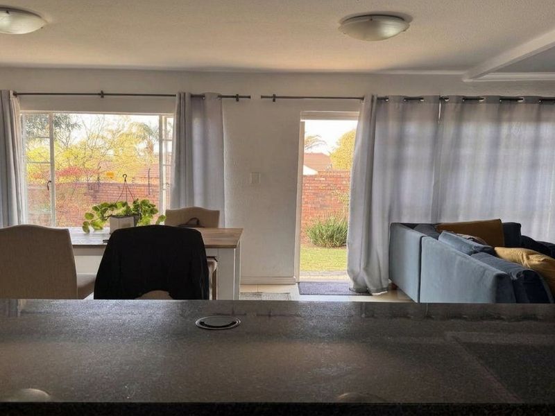 Open plan living and dining area featuring a granite breakfast bar, large windows, and direct access to the rear garden through a sliding door.