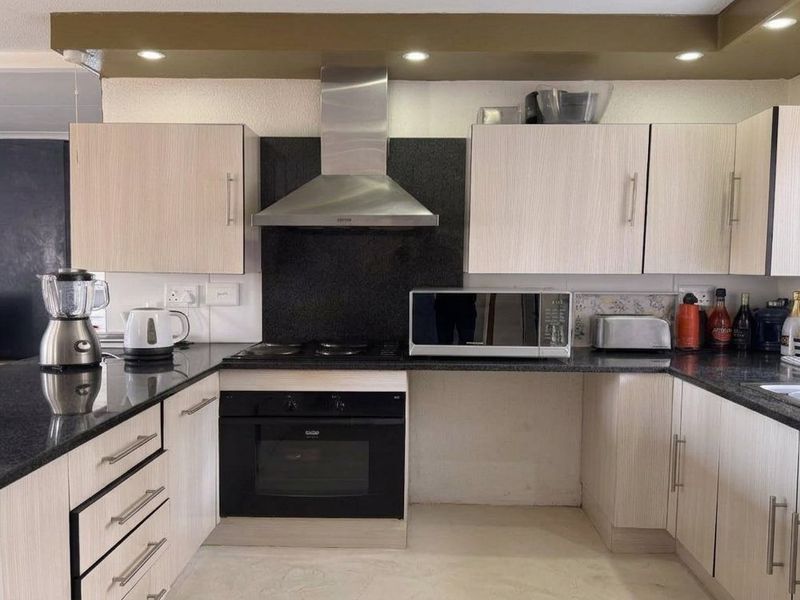Modern kitchen featuring granite countertops, light wood-finish cabinetry, built-in oven, electric hob, and a stainless steel extractor fan.