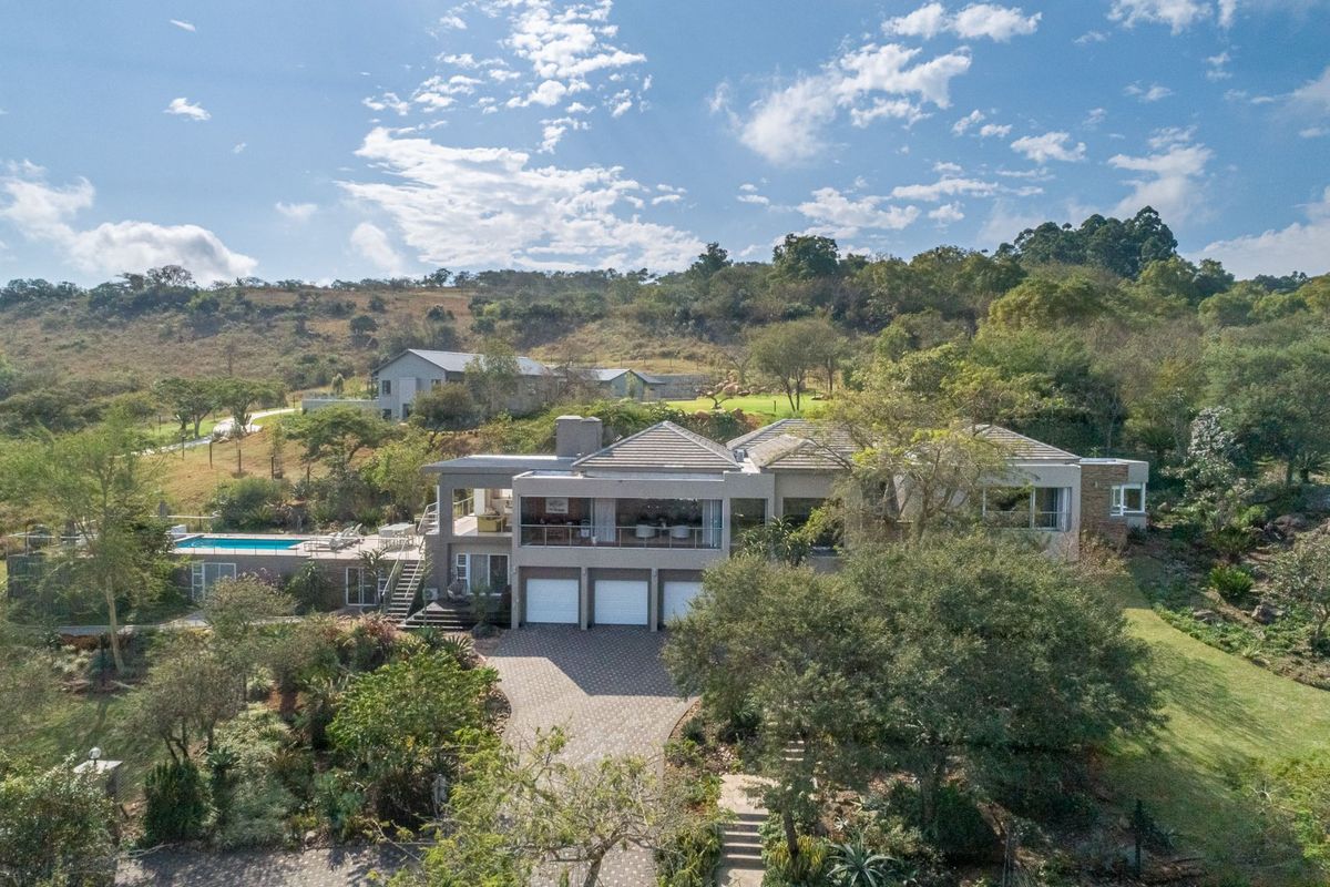 Aerial view of a large multi-level residential property featuring a triple garage, swimming pool, and expansive landscaped grounds in a scenic setting.