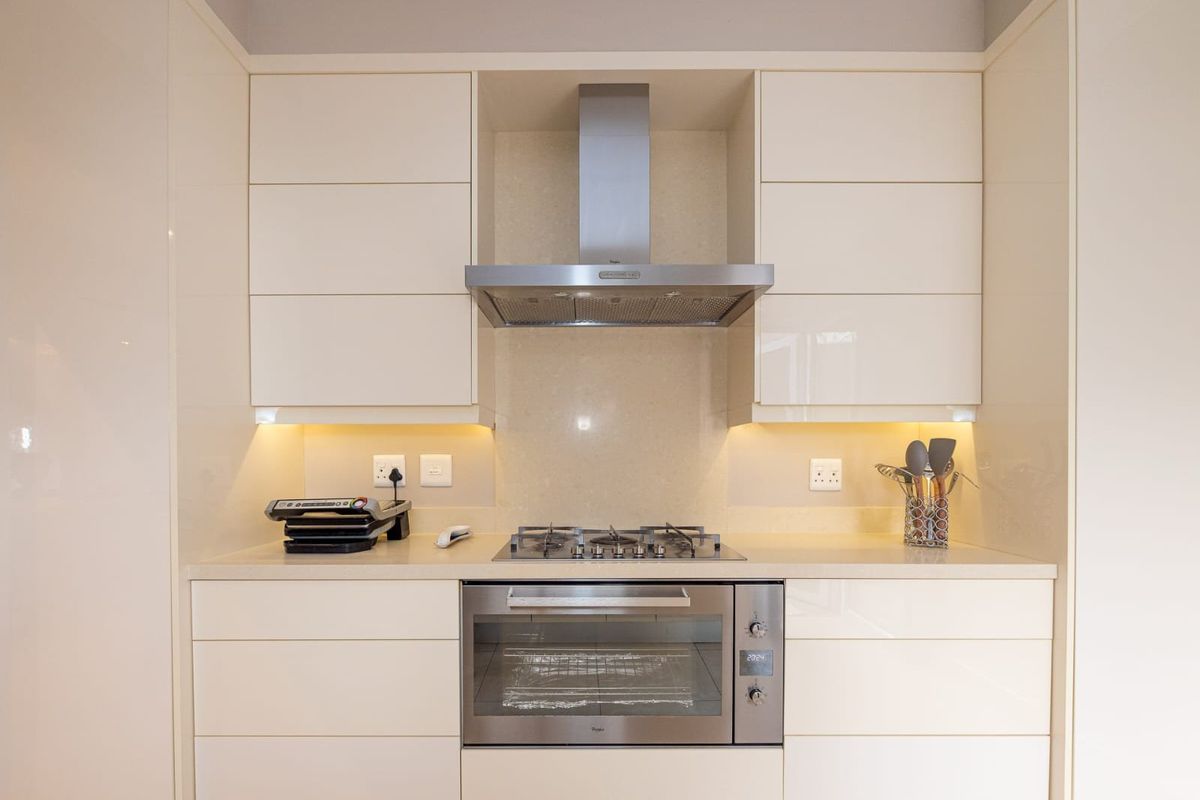 Modern kitchen featuring high-gloss cabinetry, stone countertops, a built-in oven, gas hob, and stainless steel extractor fan with integrated under-cabinet lighting.