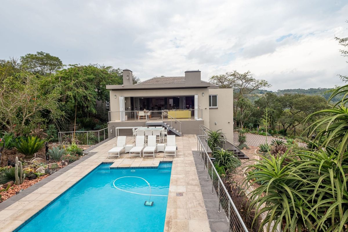Rear view of the property featuring a swimming pool, stone deck, stainless steel balustrades, and a covered patio with bi-fold doors leading to the interior.