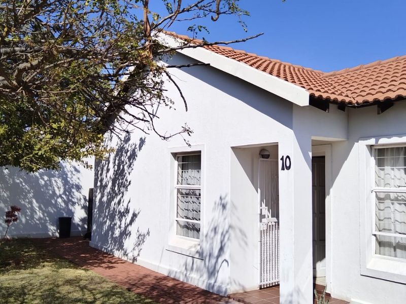 Front facade of a residential house featuring a terracotta tiled roof, white exterior walls, and a brick paved entrance walkway.