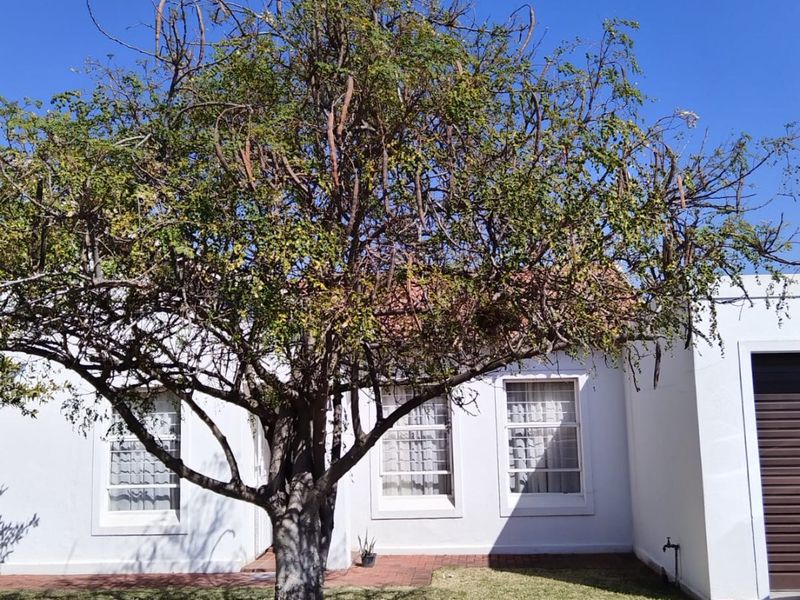 Front view of a residential property featuring a white facade, tiled roof, garage, and a well-maintained front lawn with a mature tree.