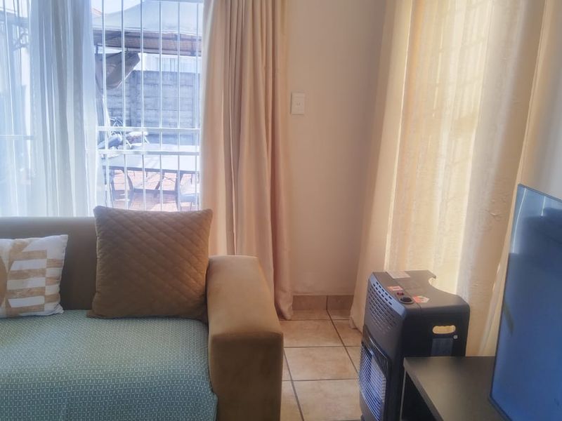 A living room featuring tiled flooring, natural light through large windows with security bars, and access to an outdoor area via a sliding door.