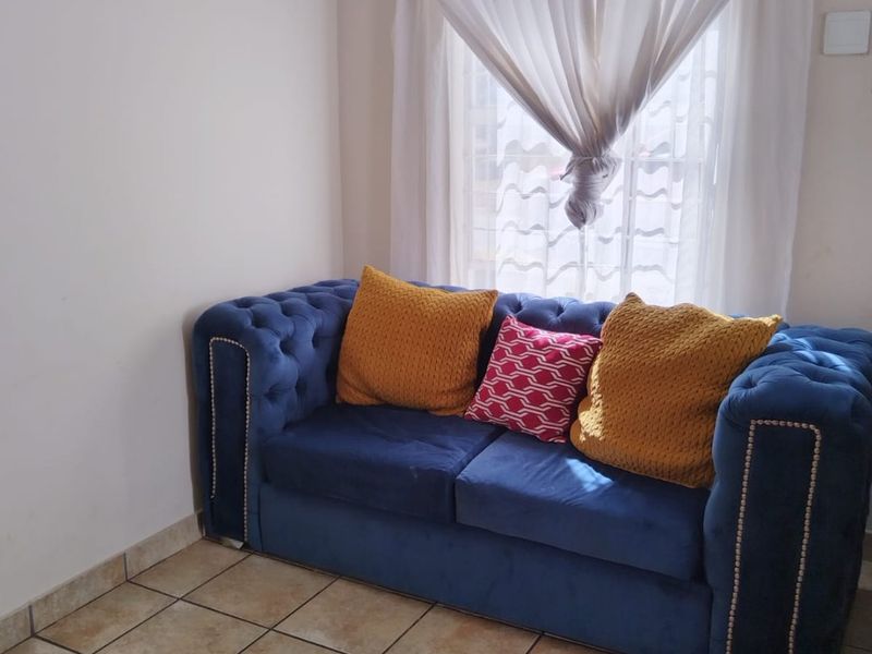 A living room area featuring ceramic floor tiles, coved ceiling cornicing, and a window with natural light.