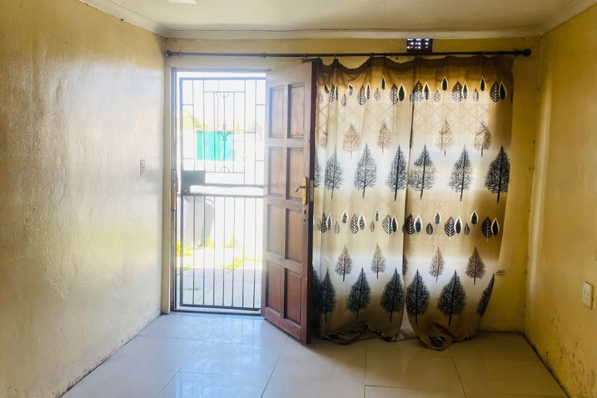 An empty living room featuring tiled flooring, a security gate entrance, and ceiling lighting, requiring cosmetic updates to the walls and ceiling.