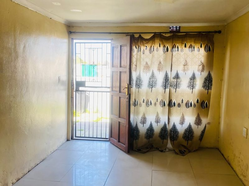 An empty living room featuring tiled flooring, a security gate entrance, and ceiling lighting, requiring cosmetic updates to the walls and ceiling.