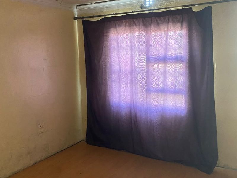 An empty bedroom featuring laminate flooring, ceiling tiles, and a window with a curtain rod, requiring cosmetic updates to improve its condition.