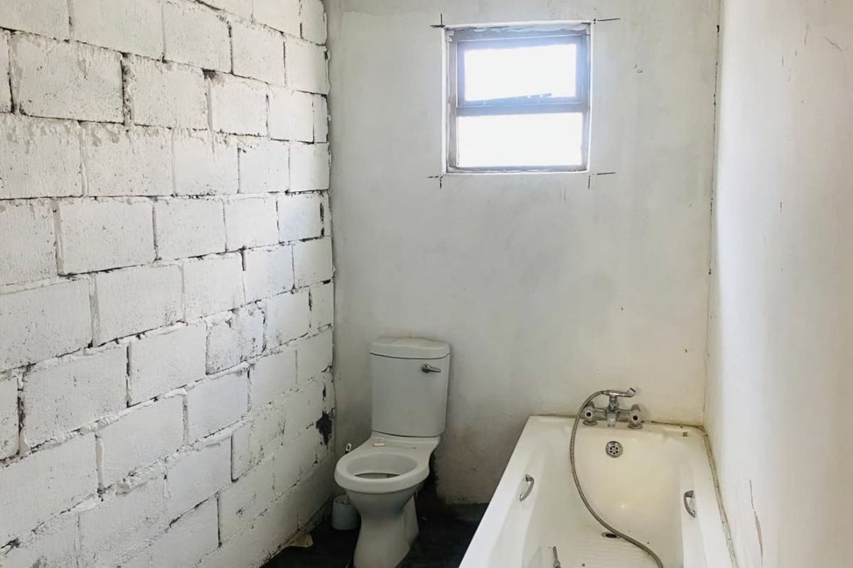 A basic bathroom in need of renovation, featuring a standard toilet and bathtub with unfinished walls and flooring.