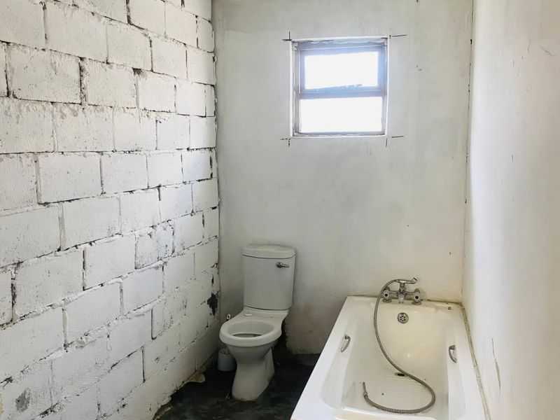 A basic bathroom in need of renovation, featuring a standard toilet and bathtub with unfinished walls and flooring.