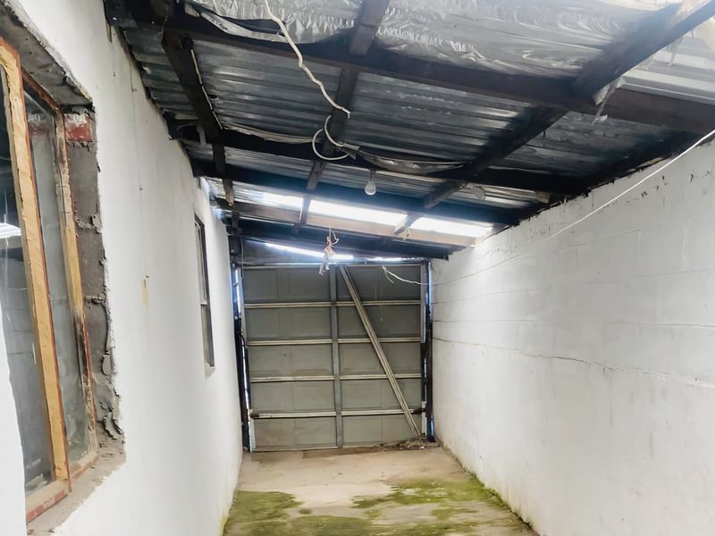 A detached garage space featuring a corrugated metal roof, concrete flooring, and a sectional door, currently requiring significant structural maintenance and repair.