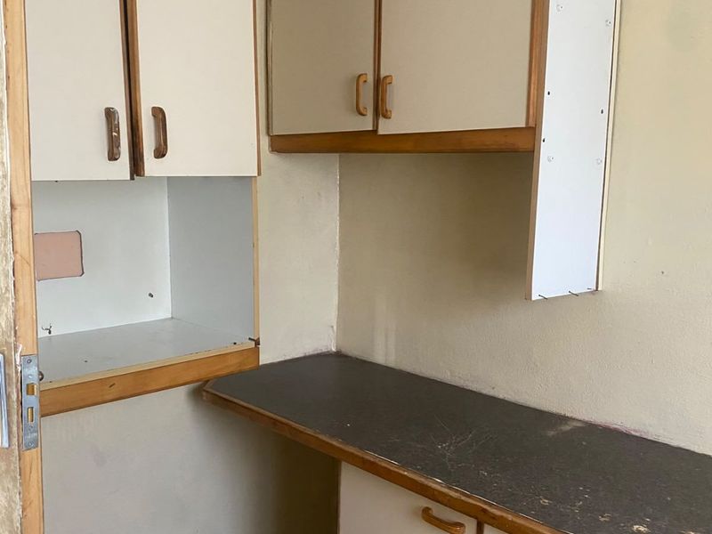 A small, dated scullery or utility area featuring worn laminate cabinetry and countertops, requiring cosmetic updates and repairs to improve functionality.