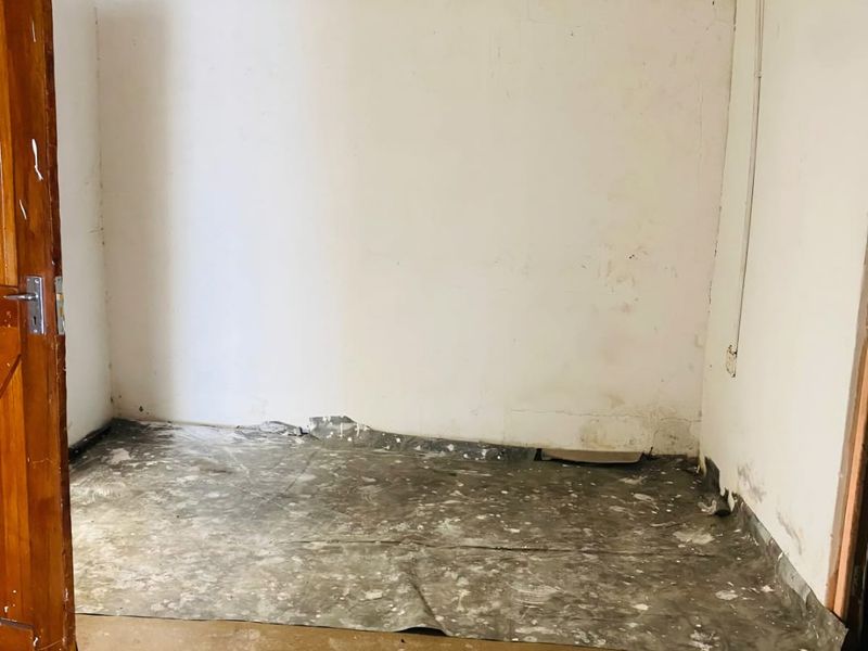 An empty room in poor condition requiring significant renovation, featuring exposed electrical conduit, damaged wall finishes, and water-stained ceilings.