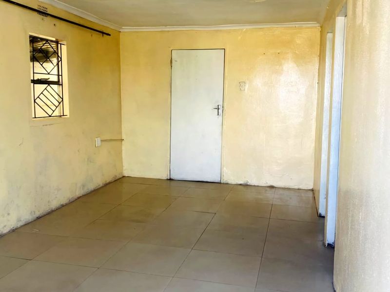 An empty living area featuring tiled flooring, a security gate on the window, and a ceiling in need of repair and repainting.