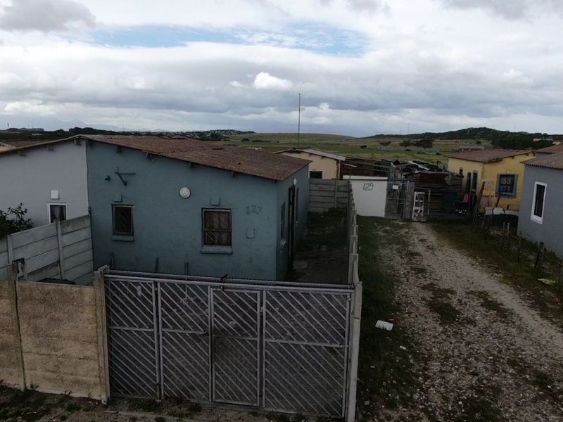 An elevated view of a residential property featuring a fenced yard, metal security gate, and a structure with a corrugated metal roof.