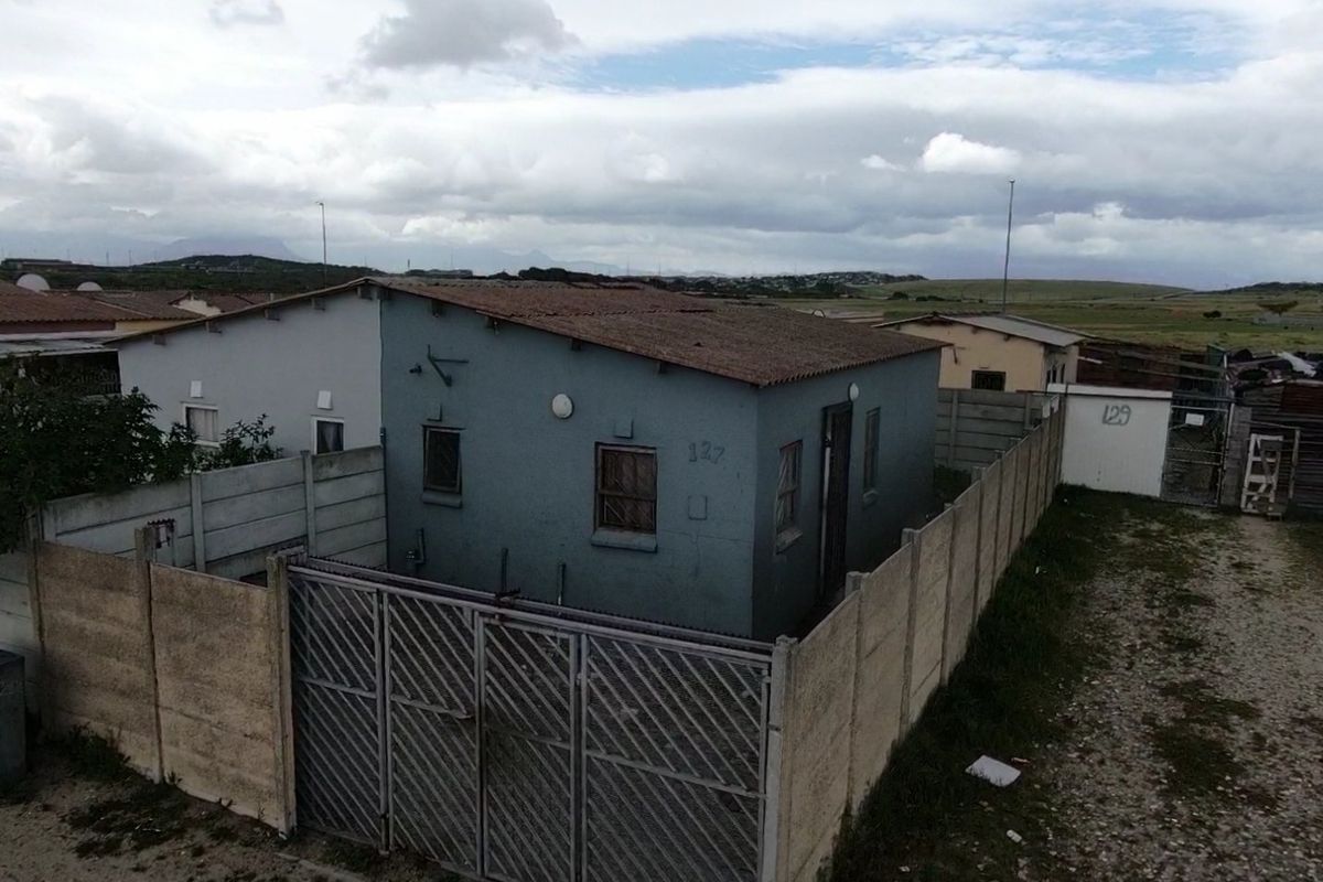 A detached single-story house featuring a tiled roof, security bars on windows, and a fully enclosed yard with a metal security gate.