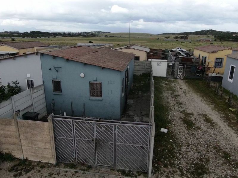 Aerial view of a residential property featuring a blue exterior, corrugated metal roof, and a fenced yard with an unpaved driveway.