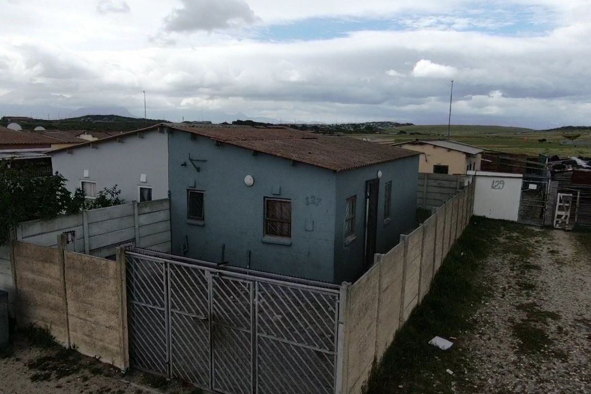 Aerial view of a detached residential property featuring a corrugated metal roof, security fencing, and a gated entrance in a suburban setting.