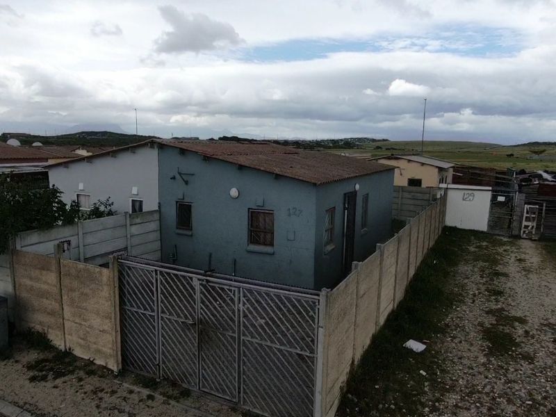 Aerial view of a detached residential property featuring a corrugated metal roof, security fencing, and a gated entrance in a suburban setting.