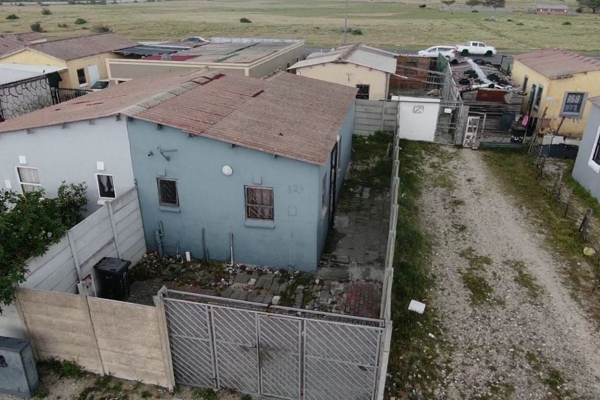 Aerial view of a residential property featuring a blue exterior, corrugated metal roof, paved yard area, and precast concrete boundary walling.