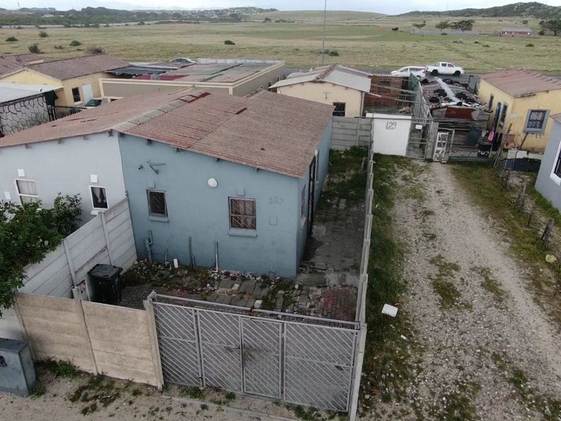 Aerial view of a residential property featuring a blue exterior, corrugated metal roof, paved yard area, and precast concrete boundary walling.