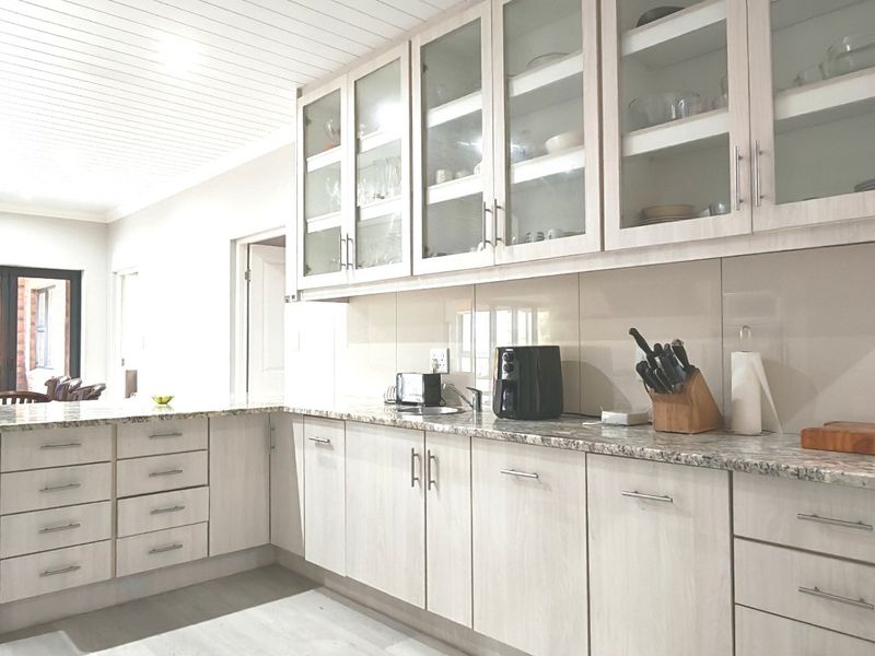 Open-plan kitchen featuring light-toned cabinetry, granite countertops, and a glass-fronted display cabinet, seamlessly flowing into the adjacent dining area.