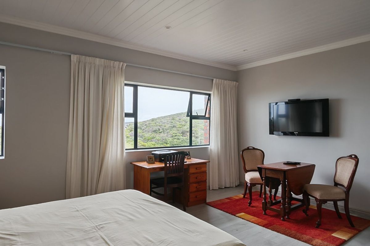 A spacious bedroom featuring a tongue and groove ceiling, aluminium window frames, and a wall-mounted television with scenic views.