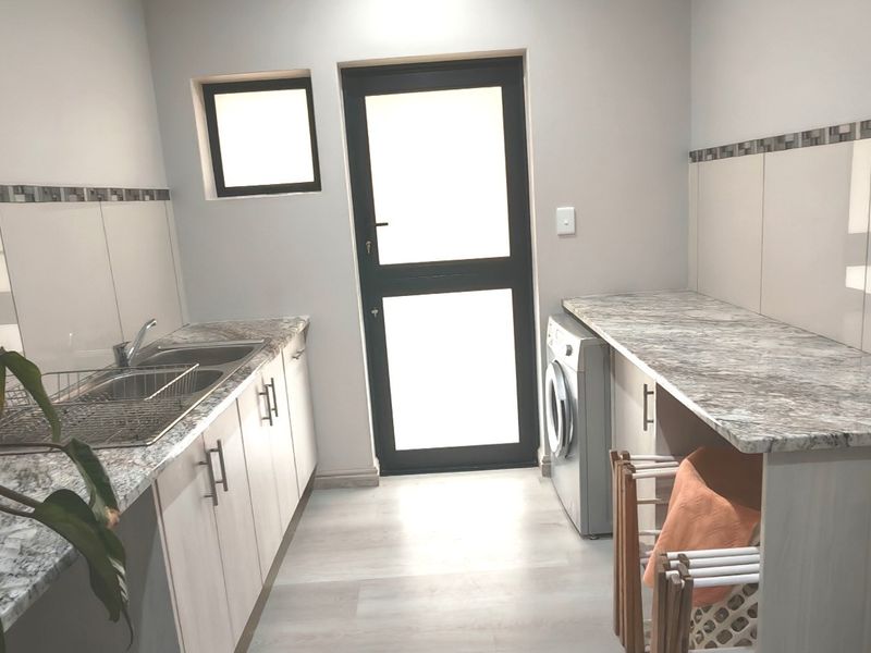 A clean and functional laundry room featuring built-in cabinetry, granite-look countertops, a stainless steel sink, and direct access to the exterior.