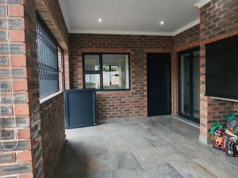 A covered patio area featuring exposed brick walls, tiled flooring, and modern aluminium fixtures, offering a versatile outdoor space for relaxation or entertainment.
