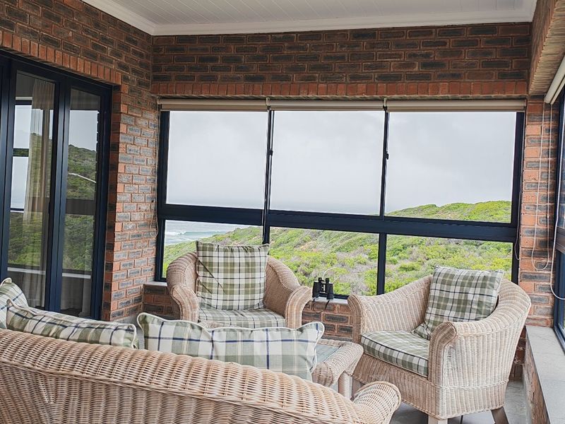 Enclosed patio featuring exposed brick walls, large aluminium-framed windows, and sliding doors, offering scenic views of the surrounding landscape.