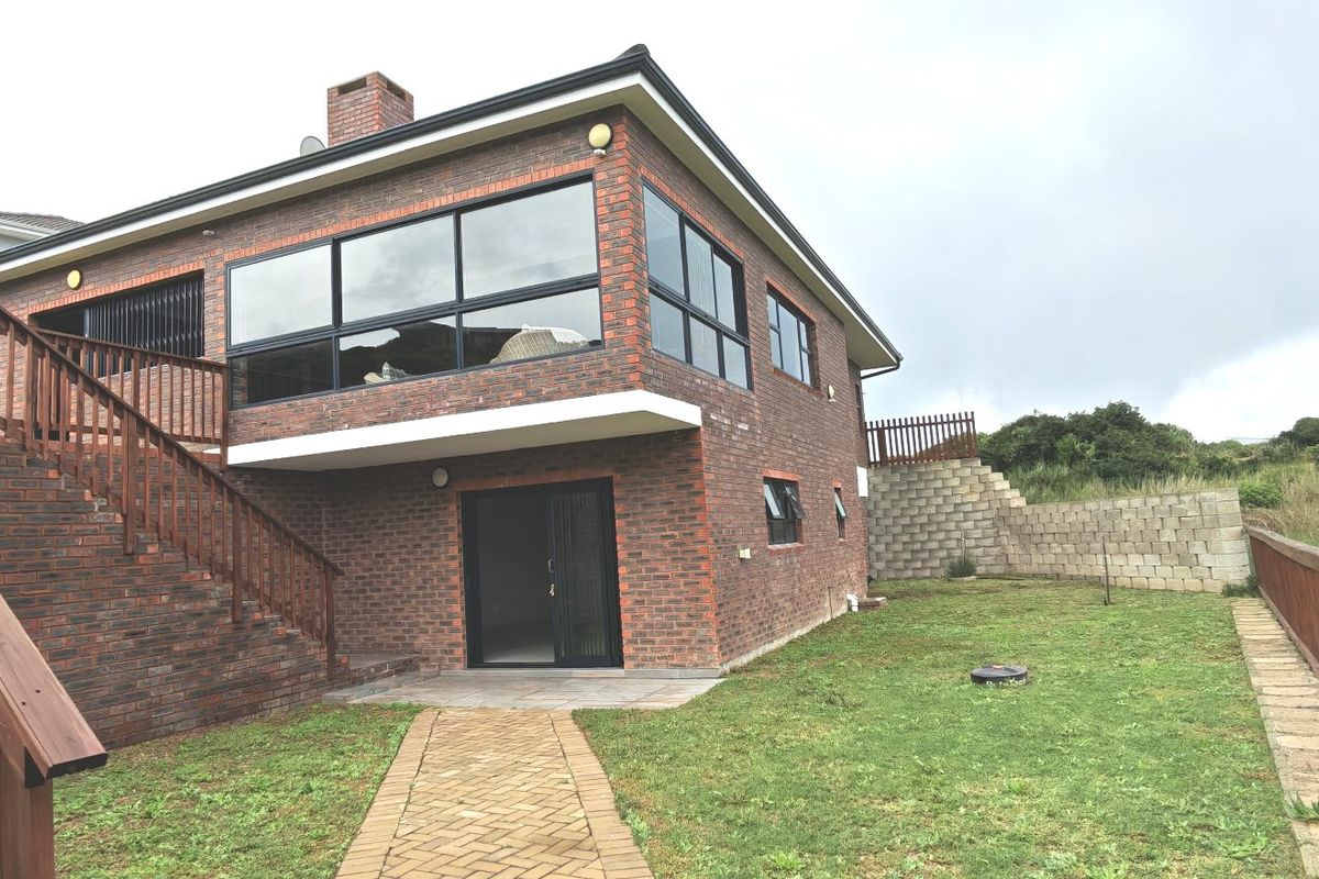 Rear view of a double-story brick house featuring a timber staircase, paved walkway, and a spacious backyard with a retaining wall.