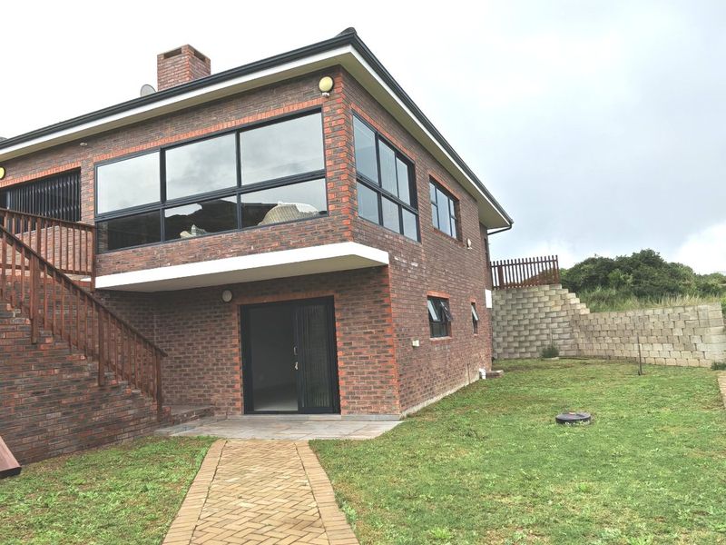 Rear view of a double-story brick house featuring a timber staircase, paved walkway, and a spacious backyard with a retaining wall.