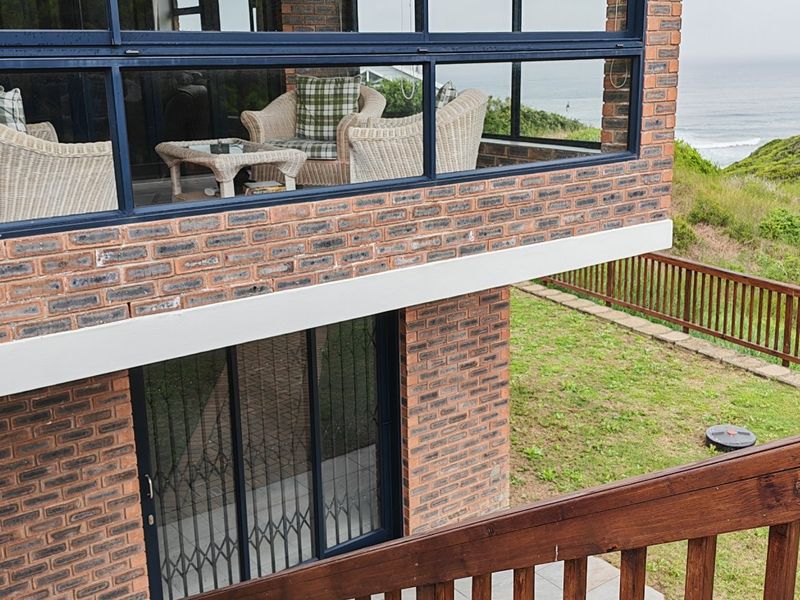 Rear view of a face brick house featuring an enclosed balcony with ocean views, a lower patio area, and wooden balustrades.