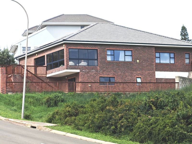 A multi-level face brick house featuring a tiled roof, aluminium window frames, and a metal balustrade, situated on a sloped corner lot.