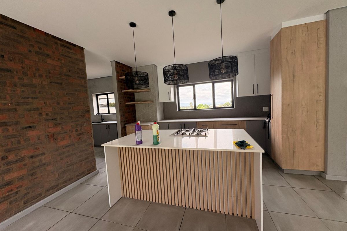 Modern kitchen featuring a central island with a gas hob, exposed brick accents, sleek cabinetry, and contemporary pendant lighting.