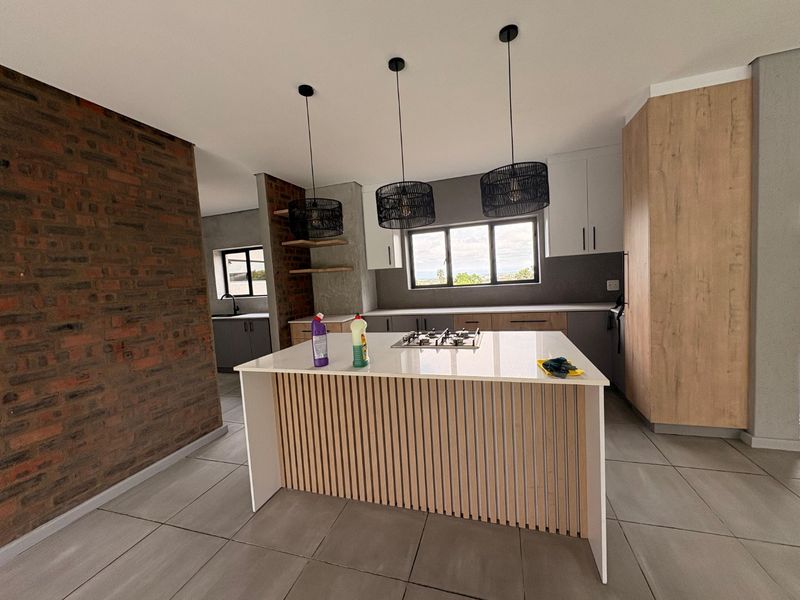 Modern kitchen featuring a central island with a gas hob, exposed brick accents, sleek cabinetry, and contemporary pendant lighting.