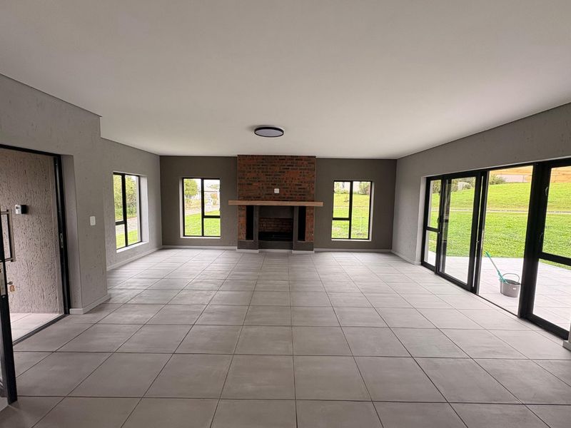 Spacious, modern living area featuring large aluminium sliding doors, tiled flooring, and a central brick fireplace with a timber mantelpiece.