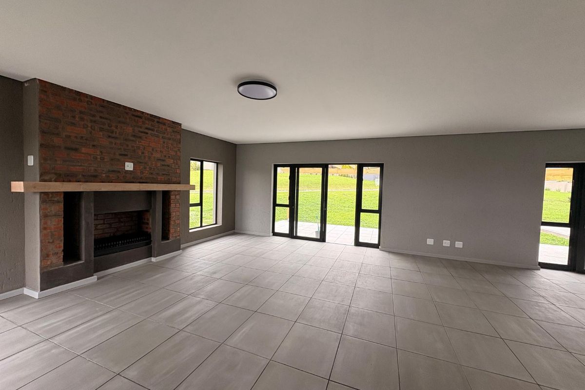 Spacious, modern living area featuring a prominent brick fireplace with timber mantel, large format floor tiles, and expansive glass doors opening to the garden.